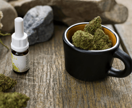 una tazza piena di fiori cannabis cbd su di un tavolo in legno, di fianco un flacone olio cbd private label